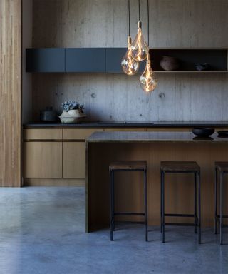 An example of modern kitchen lighting ideas showing a dark kitchen with wooden and black cabinets, marble flooring and a feature pendant light