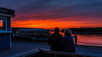 Retired couple sitting in downtown Bar Harbor, Maine in summer during bright red sunset at twilight.