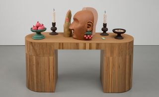 Artwork comprising wooden desk topped with decorative objects