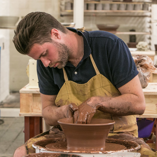 man with black tshirt and yellow apron making clay pot
