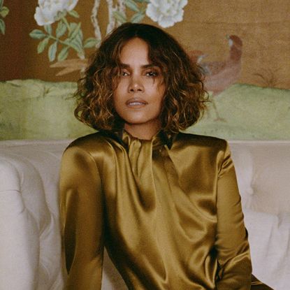 Halle Berry sits on a white sofa in a high-neck yellow satin gown by Saint Laurent