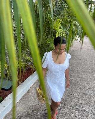 A woman wearing a white short-sleeve mini dress with a woven bag.