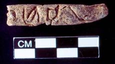 A clay artifact, about the size of a finger with engraved symbols.