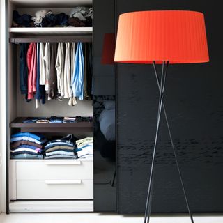 A built-in wardrobe with clothes and glossy sliding doors with a floor lamp in front of it