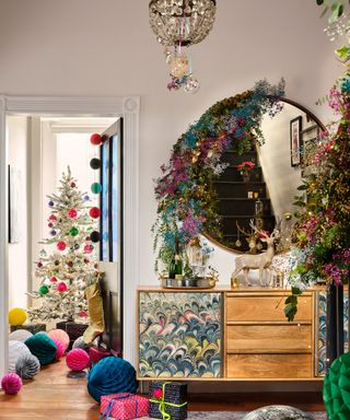 A bright and colorful Christmas hallway with chandelier, statement console table, large round gold-framed mirror and paper honeycomb decorations