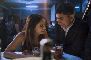 a couple (Camila Mendes as Ana, Archie Renaux as William) lean over a bar table and laugh over drinks, in the Prime Video rom-com 'Upgraded'