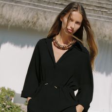 zara model wearing gathered kimino skirt in front of straw roof house