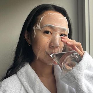 Woman wearing a sheet mask and drinking a glass of water