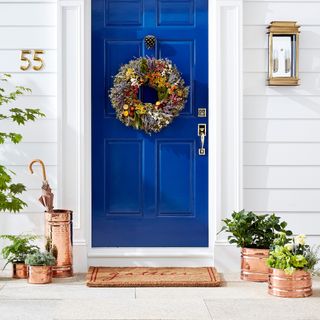 Exterior image of a white house with a deep blue door. There are five copper-colored planters around the welcome mat