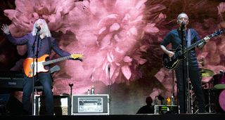 Tears For Fears' Roland Orzabal [left] and Curt Smith perform live on the band's Tipping Point tour, with pastel-coloured stage lights and video in the background.