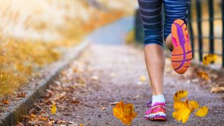 Woman running on footpath with fall leaves