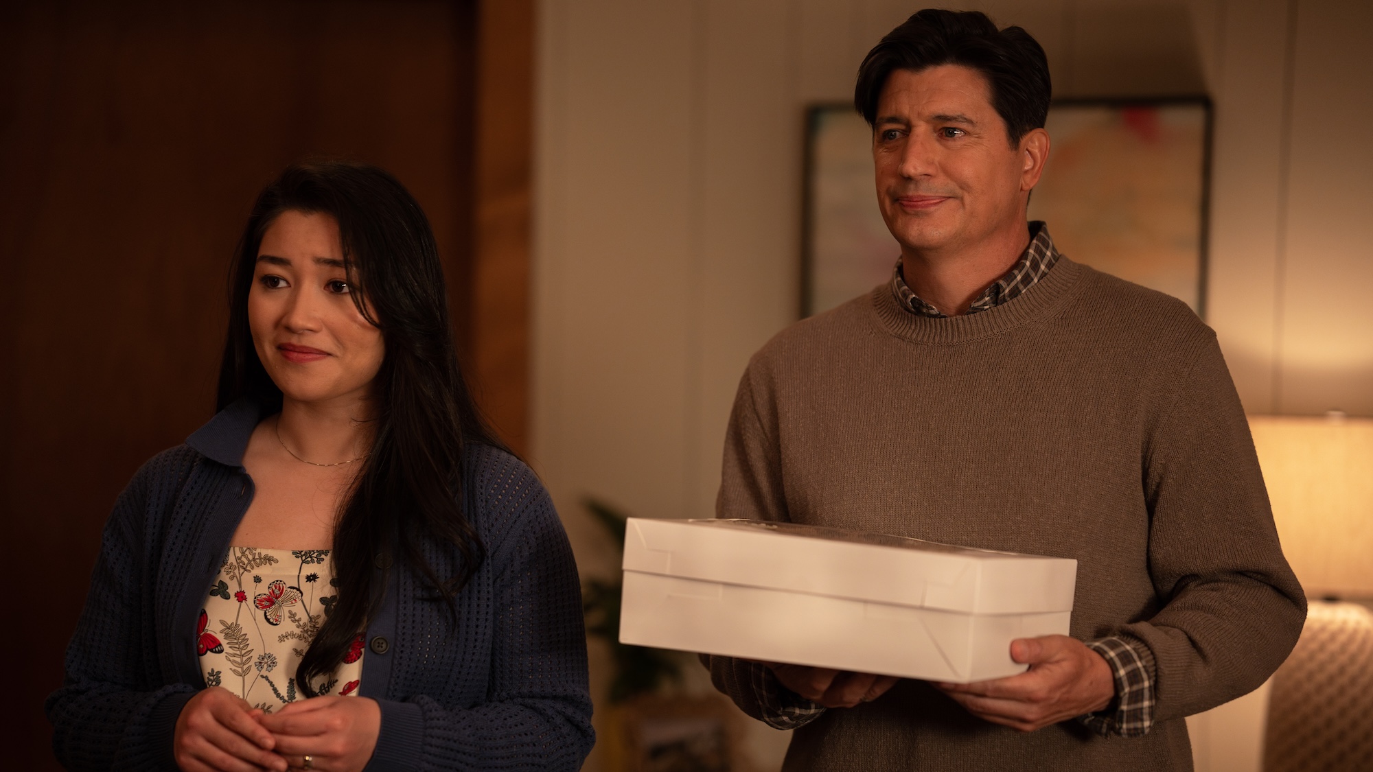 Jaylee Hamidi as Alex in shirt with butterflies on it standing next to Ken Marino's Russell wearing a tan shirt and holding a white box in Yellowjackets Season 4