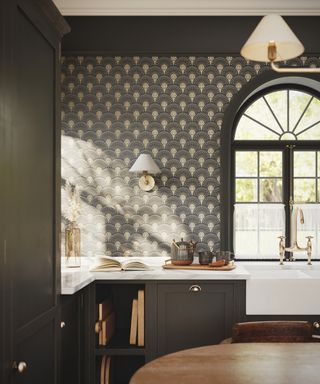 Shaker kitchen with brown cabinetry, art deco style wallpaper, arched window, marble countertops, sink, wall lights and matching pendants light, table