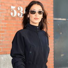 Bella Hadid wearing a cropped black bomber and wire-rim sunglasses.