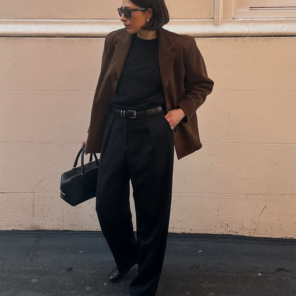 Influencer Lucy Alston wears black trousers, a black tee, and a brown suede blazer. 