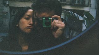 A person takes a selfie in the mirror with a Fujifilm Quicksnap disposable film camera