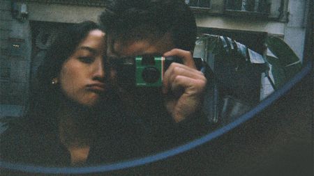 A person takes a selfie in the mirror with a Fujifilm Quicksnap disposable film camera