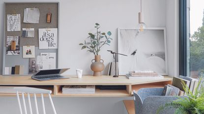 Neutral l home office with wooden desk and decorated with pin board decor, plants, and lighting