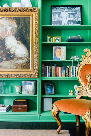 living room with bright green painted bookcase, upholstered velvet vintage chair, vintage painting with ornate gold frame