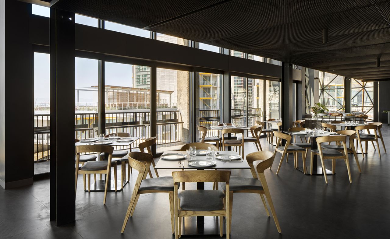 An arrangement of 4 seating per table with amix of dark grey leather and oak wood chairs and square tables dressed with plates and and glasses