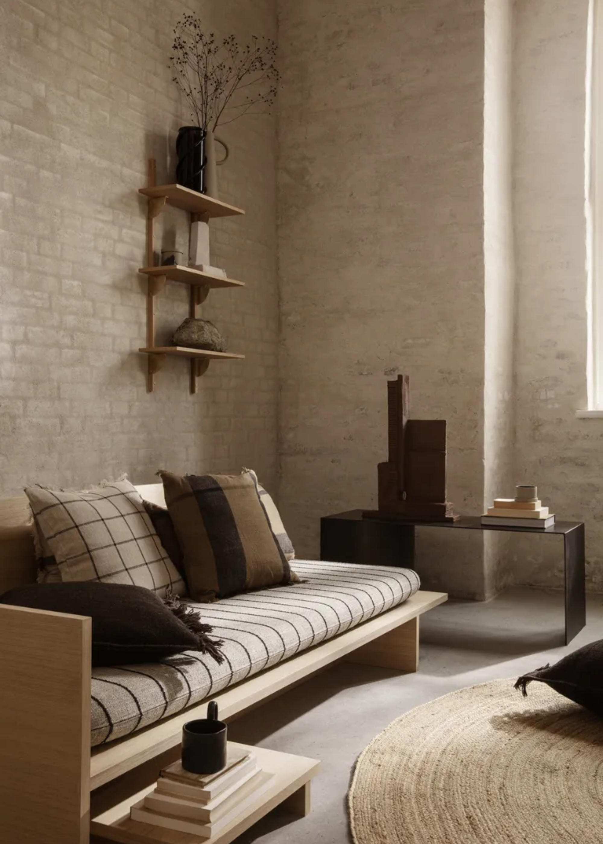 A living room with a minimalist aesthetic featuring a low-slung wood bed frame with a futon, a side table, and a round woven rug
