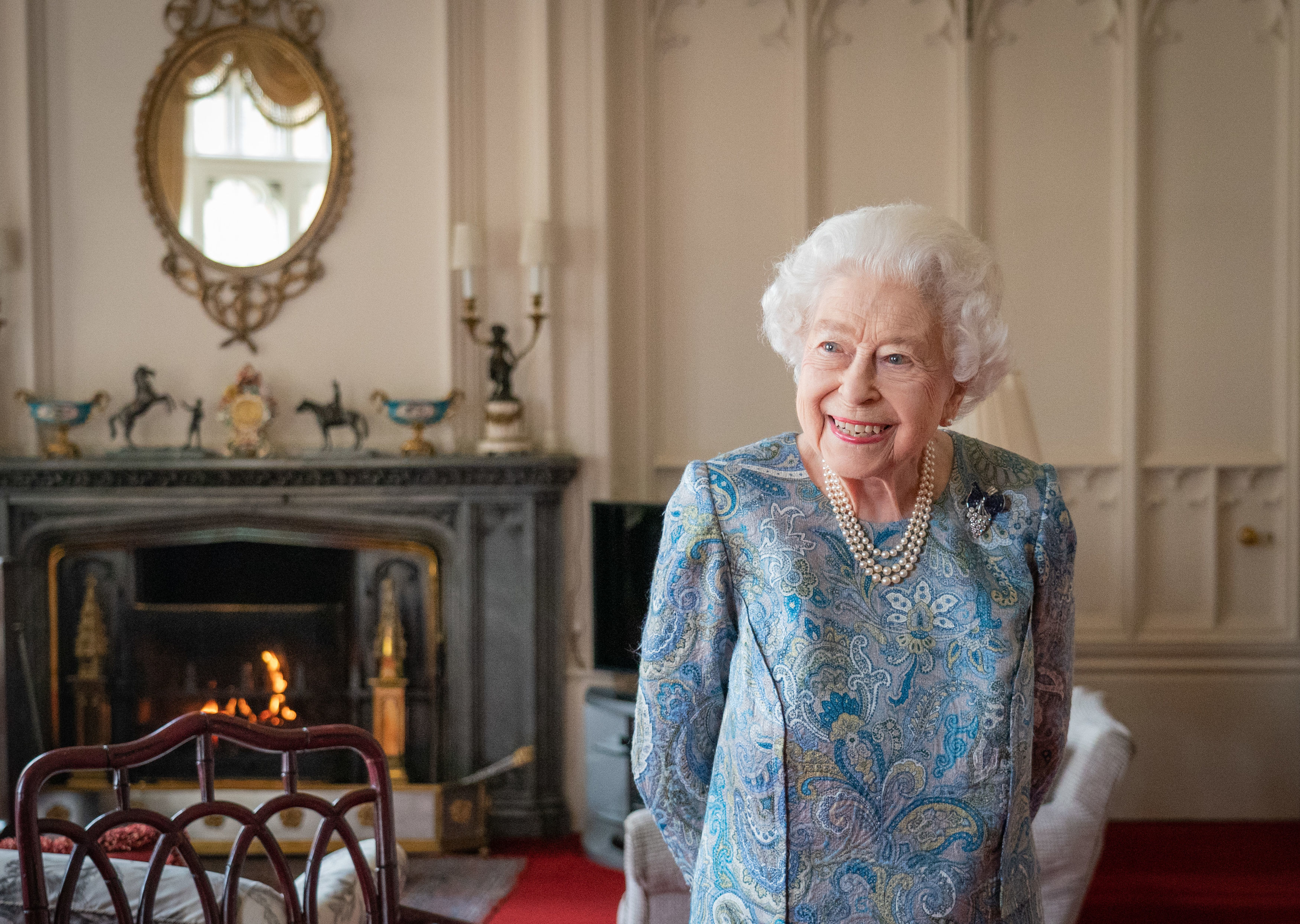 Queen Elizabeth standing in front of a fireplace and smilig