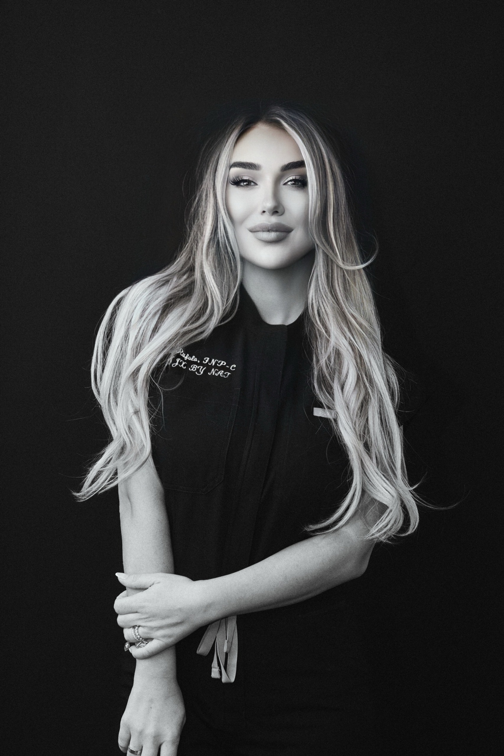 a black and white photo of a white woman with long blonde hair in black scrubs