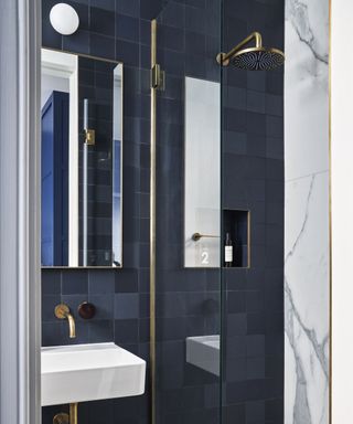 A walk-in shower with square, tonal deep blue tiles and brass fittings