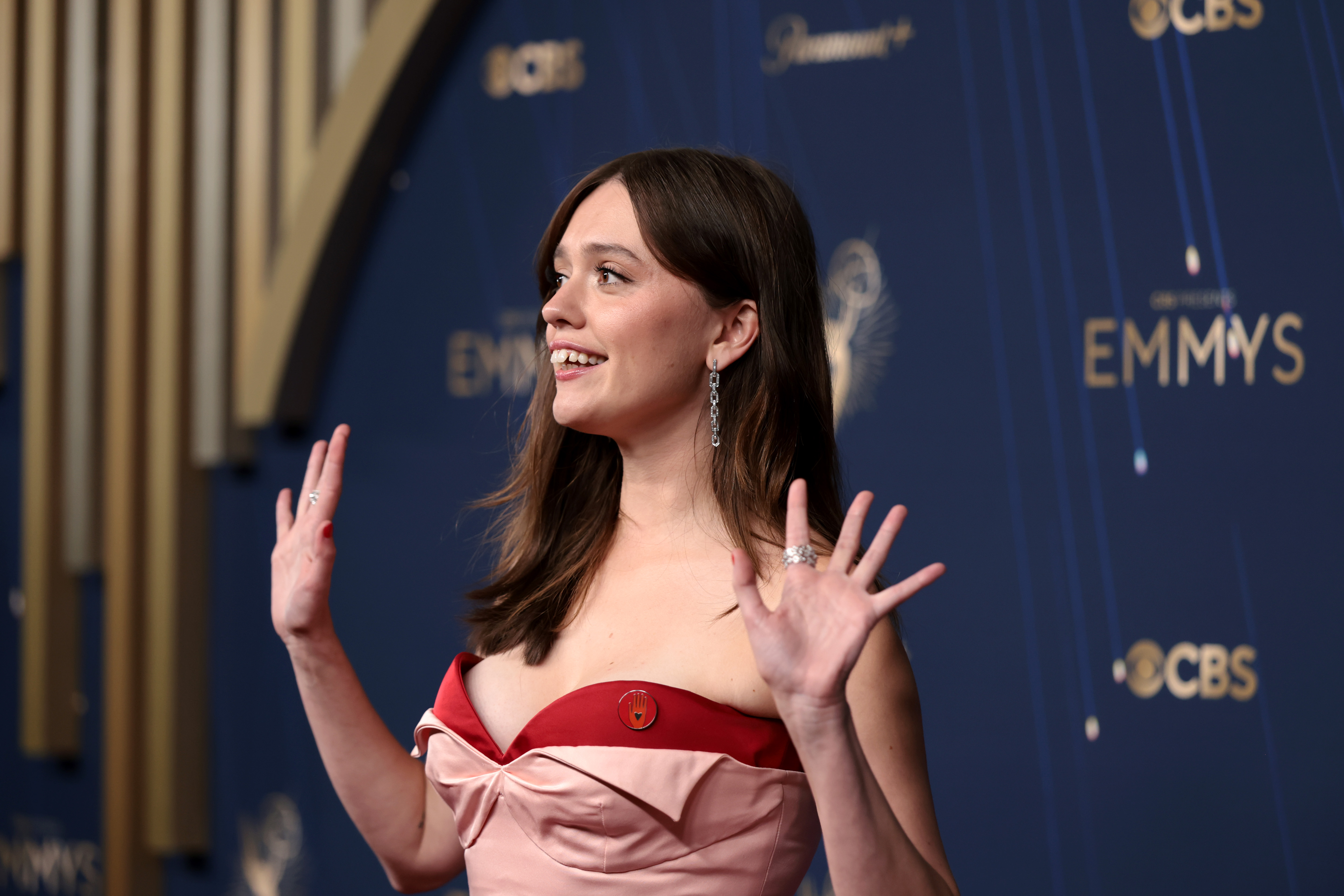 Aimee Lou Wood in a pink and red dress with her hands up