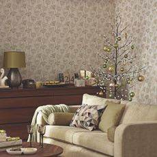 A living room with a botanical wallpaper with a twig Christmas tree in the corner decorated with green baubles