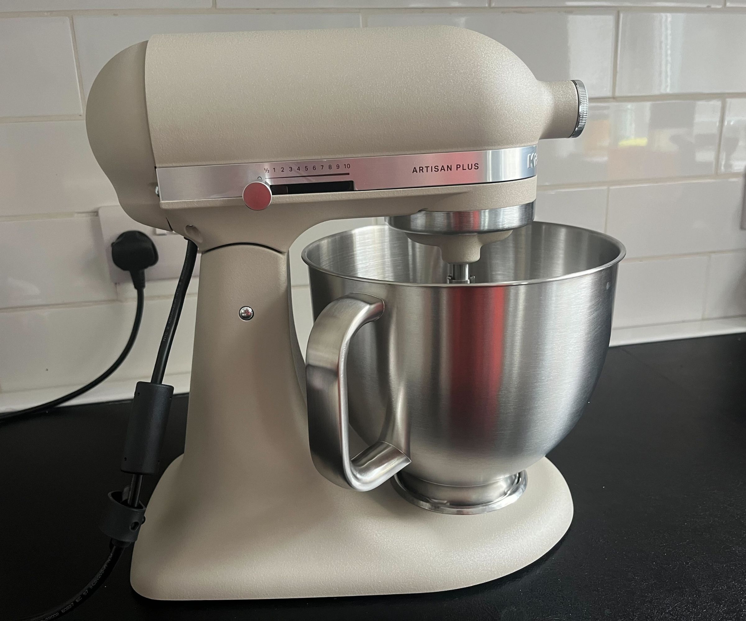 A light beige colored Kitchenaid stand mixer with a stainless steel bowl on a black kitchen counter.