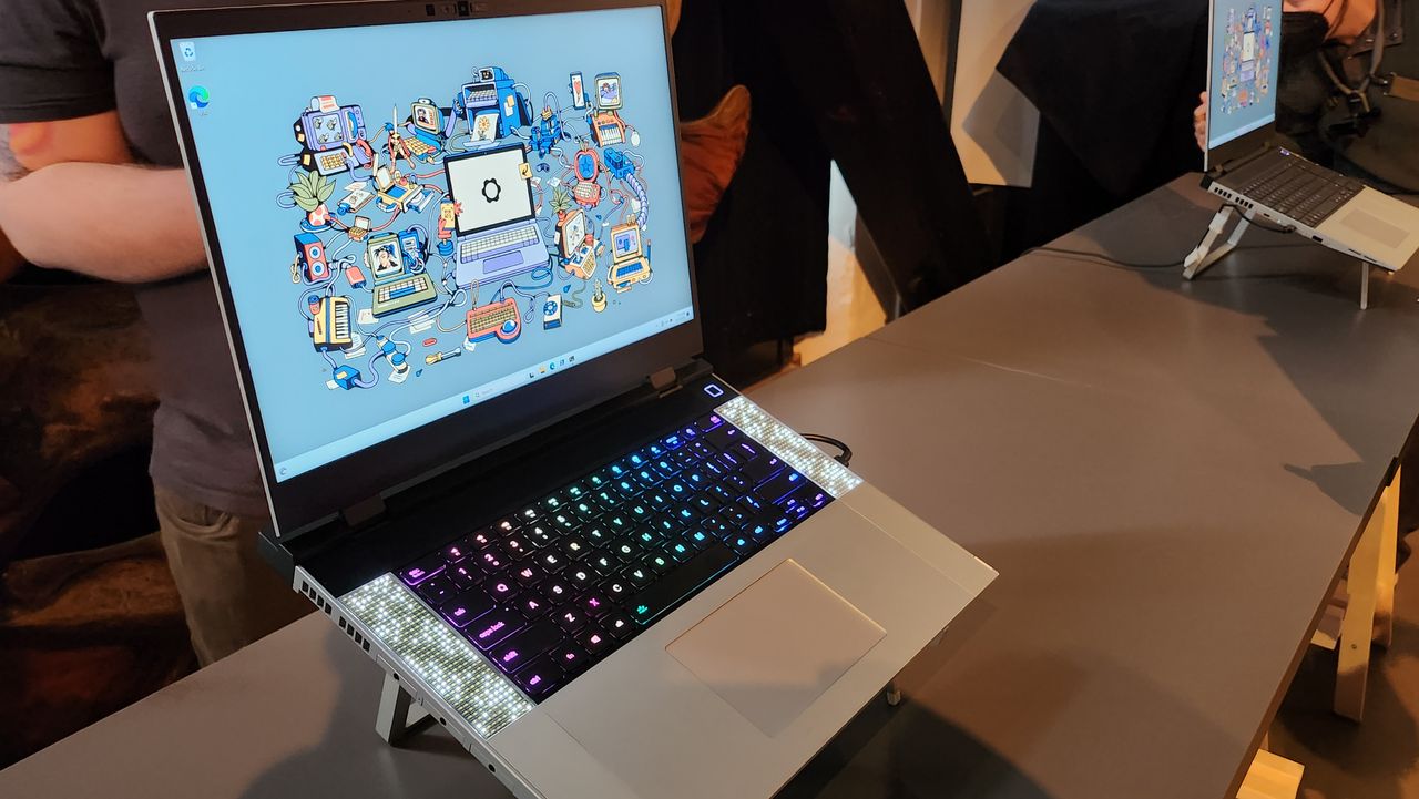 head on image of open Framework gaming laptop on presentation floor, abstract desktop background in Windows with RGB keyboard, speakers on side, chrome furnishing and slim black bezels