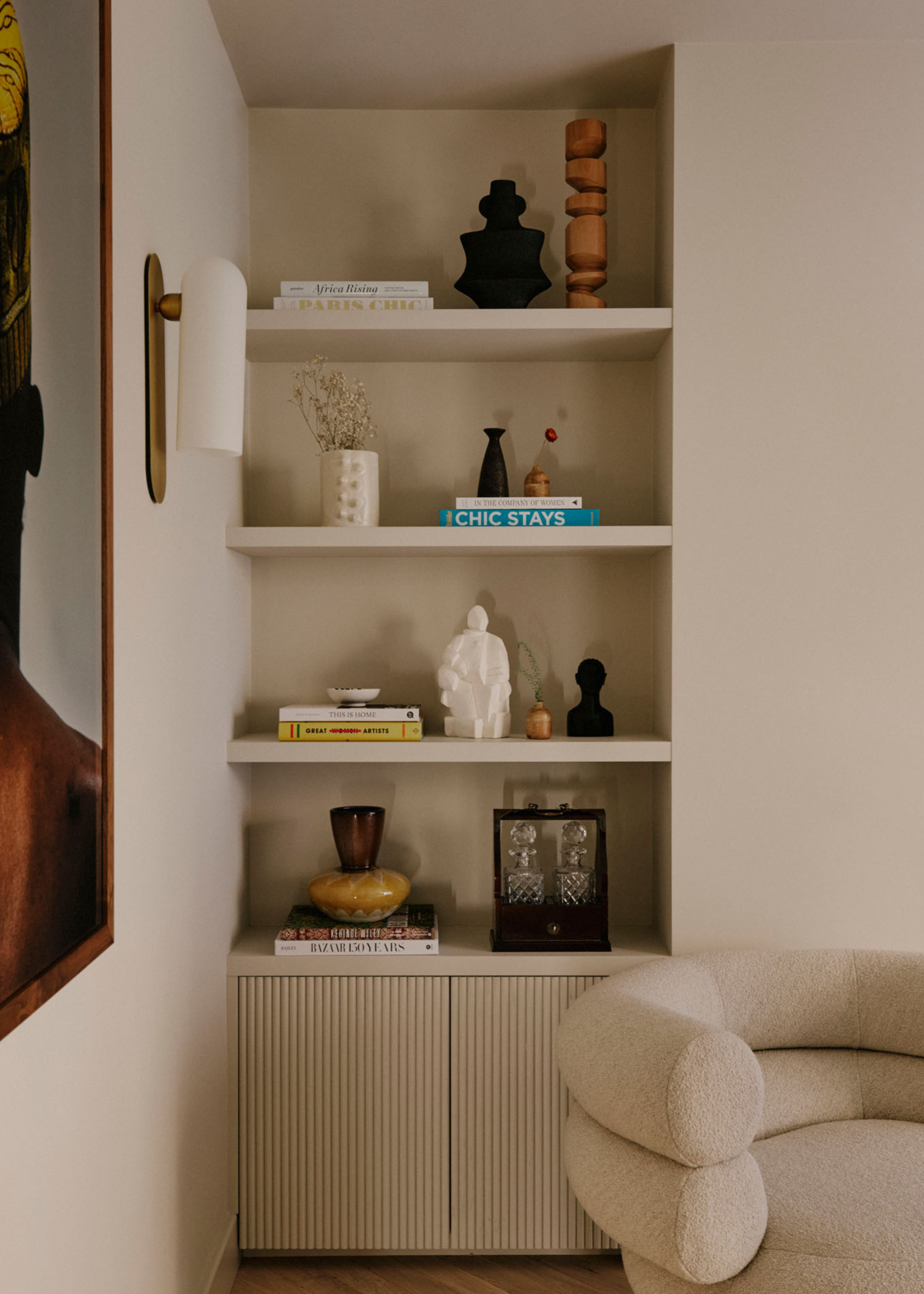 built-in alcove shelving filled with decorative items in a modern neutral space with a contemporary cream accent chair next to it and artwork on the other side
