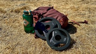 A rucksack, water bottle, and two gym plates sitting in the hilly grass on the author's hike.