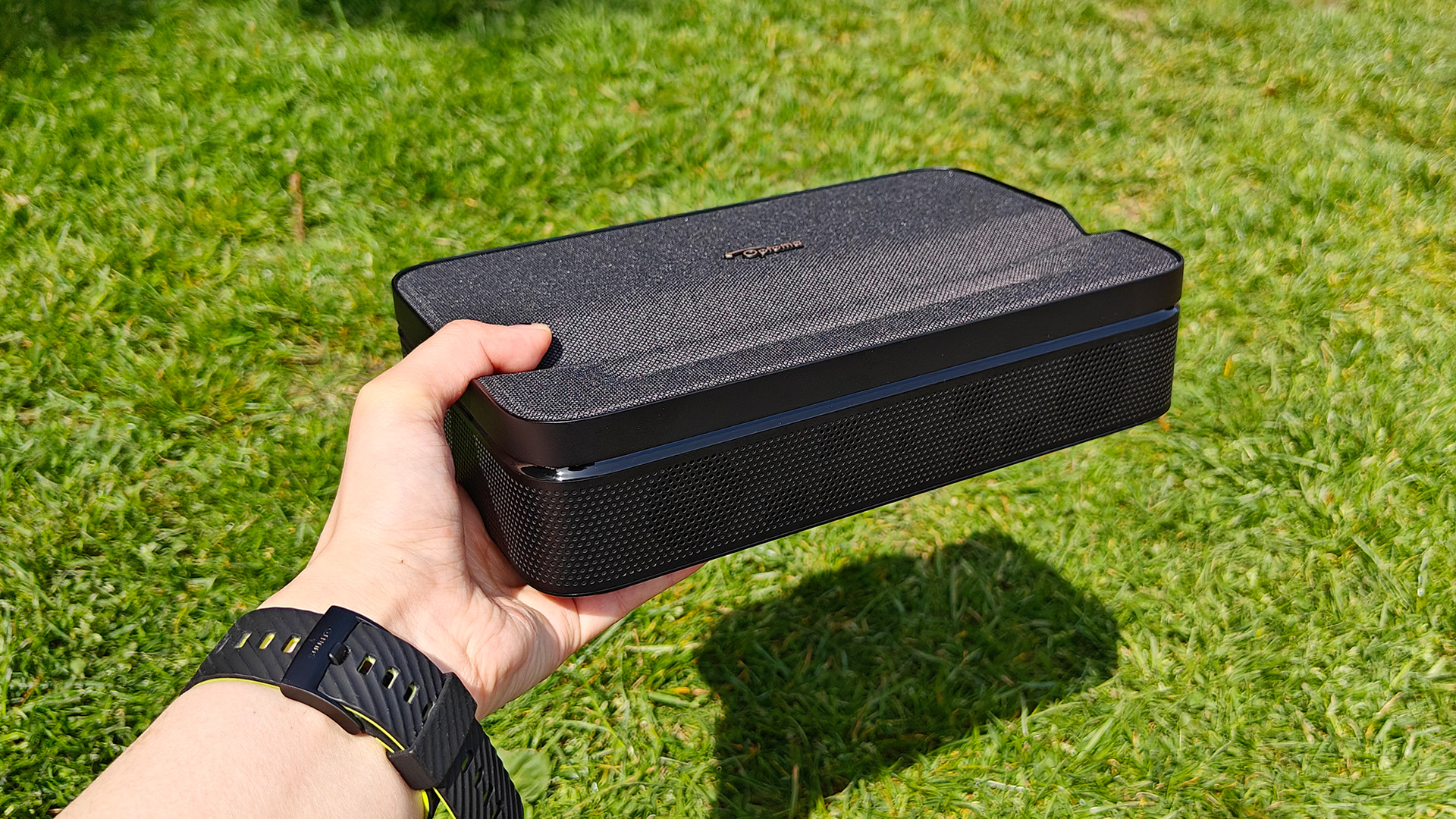 Optoma Photon Go portable UST projector held in hand over grassy lawn
