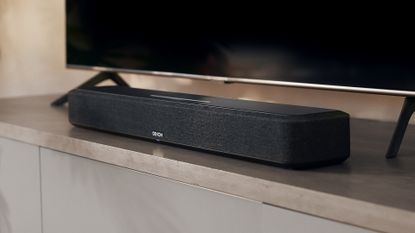 Denon Home Sound Bar 550 in front of TV on wooden surface