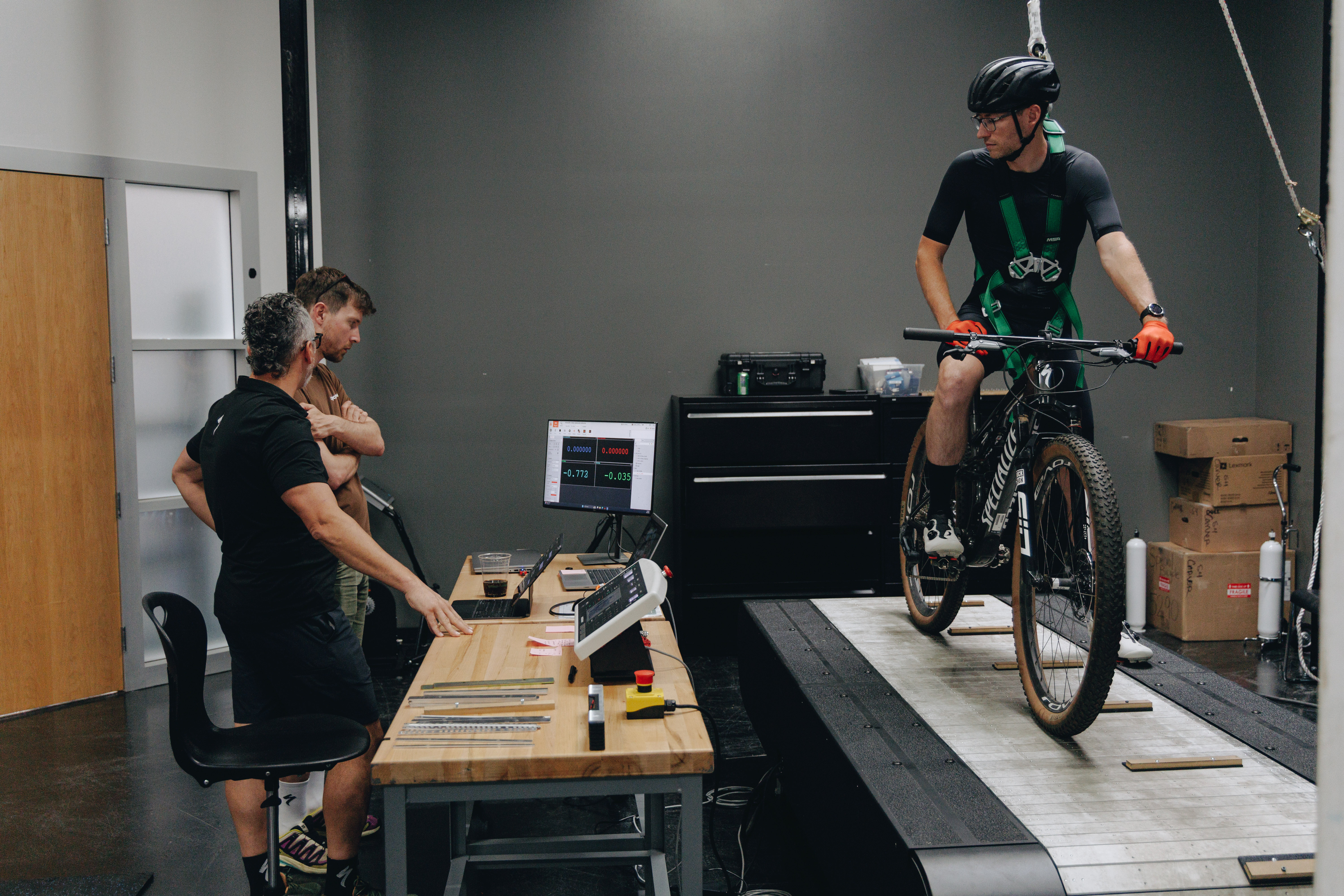 Jason Williams and Josh Croxton watch as a cyclist rides a mountain bike on a treadmill 