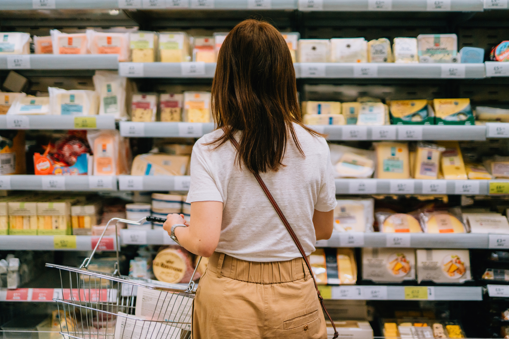 Person stands with shopping basket looking at cheese in supermarket, symbolising inflation.