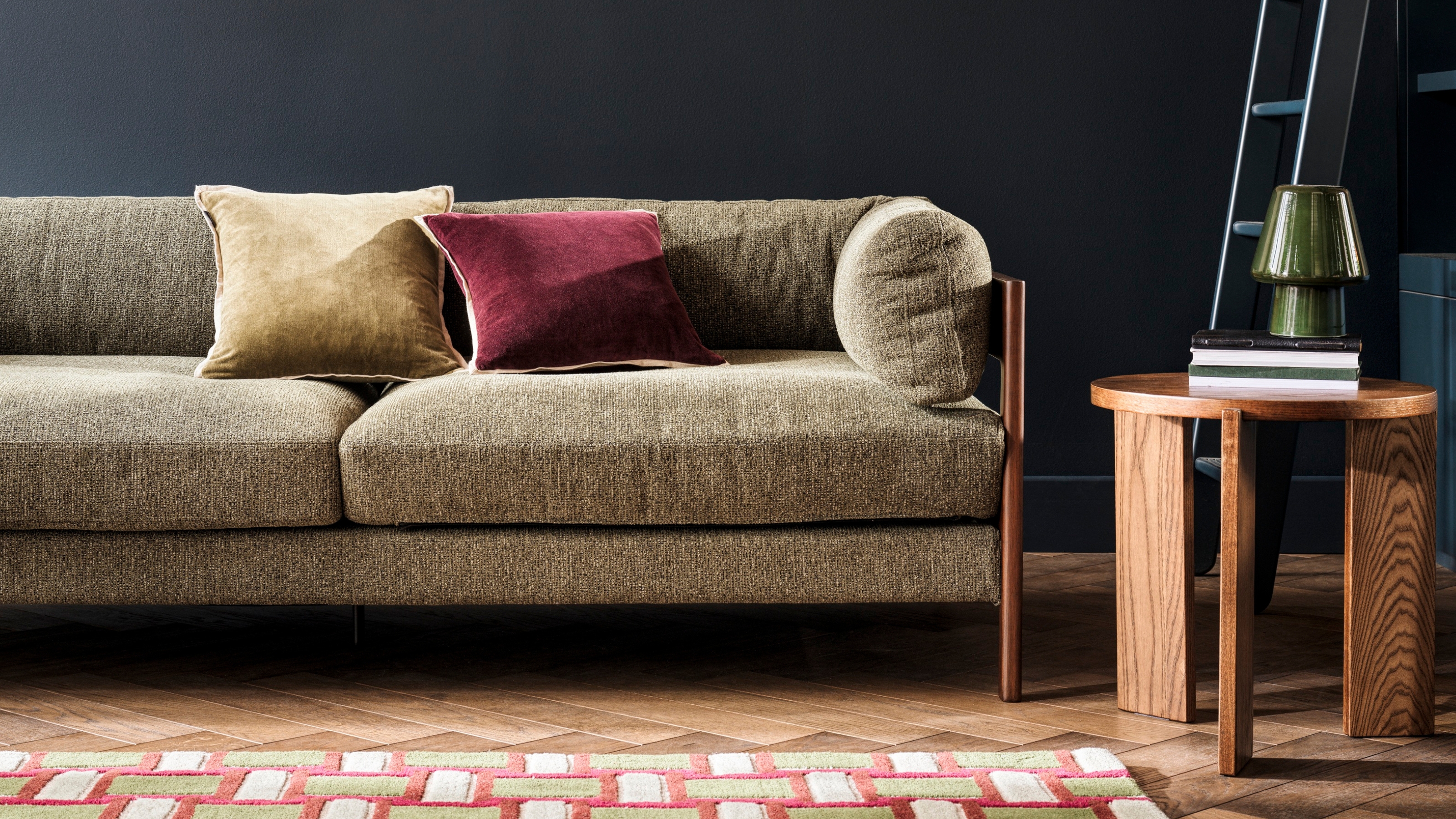 a green boucle sofa next to a wooden side table and patterned rug