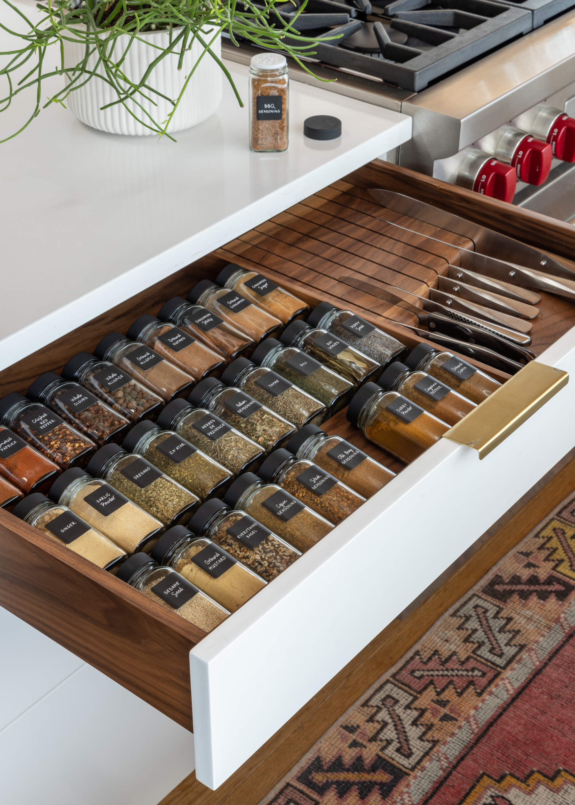 An open kitchen drawer with spice bottles and a knife rack