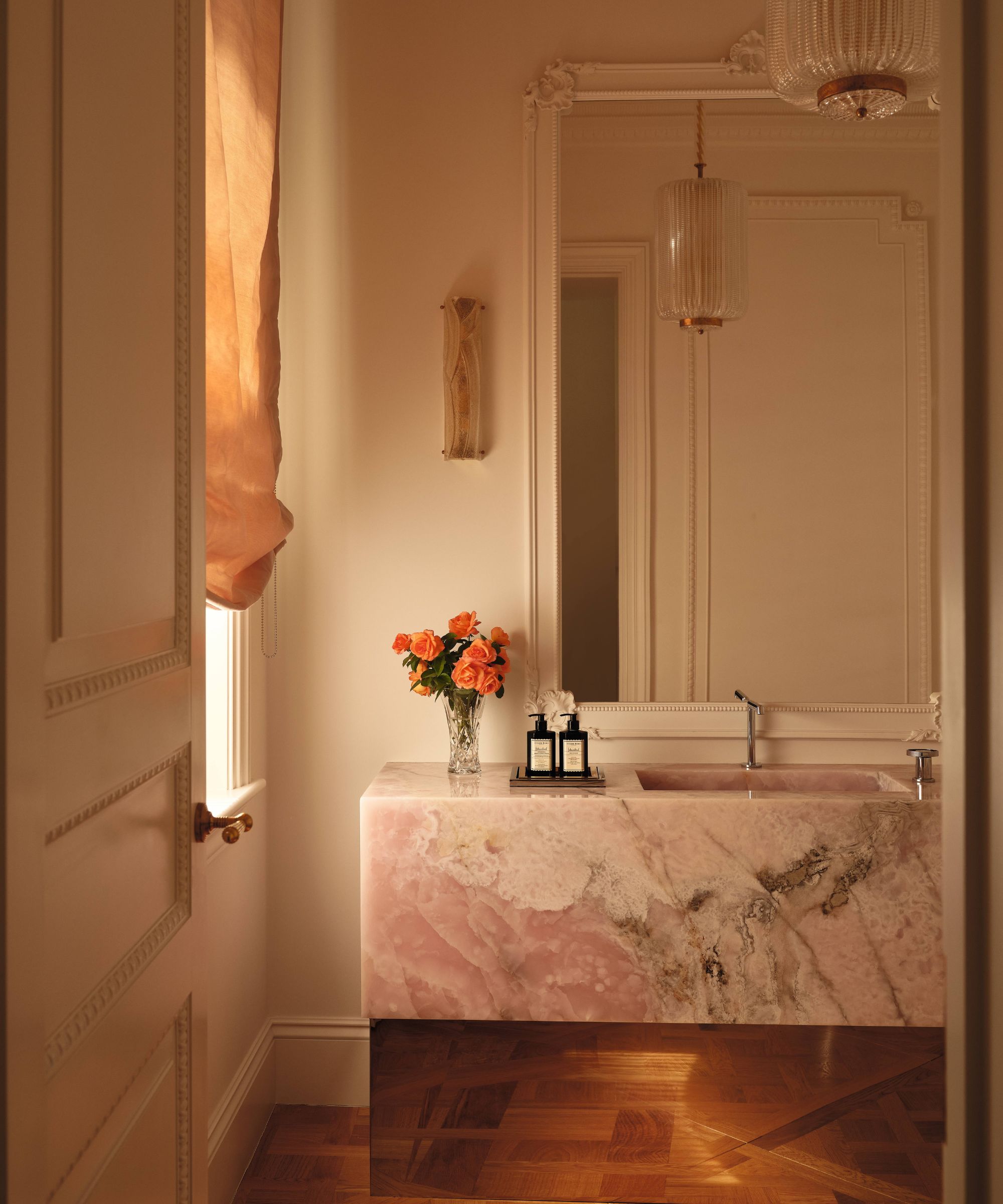 a warm moody powder room with ornate moldings and a vanity with large pink onyx stone basin