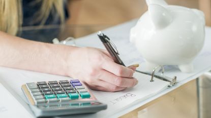 A woman writes out a budget with a calculator and piggy bank nearby.
