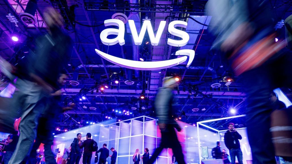 A photo of a dimly-lit conference floor with a bright white AWS sign hanging from the ceiling