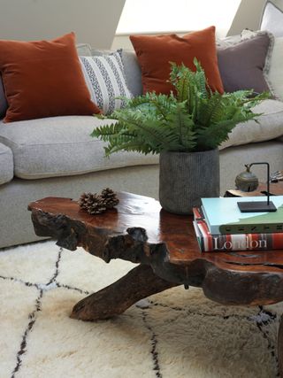 White fur rug with black diamond outlines, oil wooden stump table with wooden legs, burnt orange cushions and grey sofa