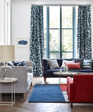 A classic coastal living room with blue patterned drapes and blue and red furnishings.