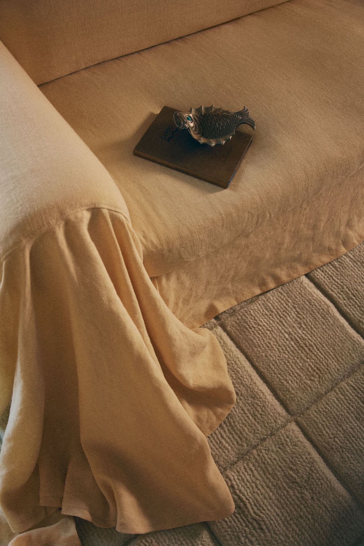 Close-up of the arm of a chair that has a light yellow, draping sofa cover on it. There is a fish-shaped dish on the seat.