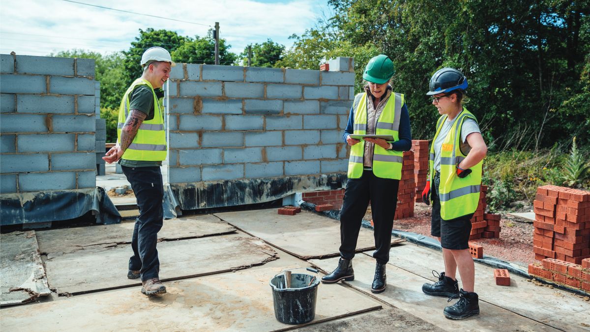 2 female construction workers on site with male looking at tablet 