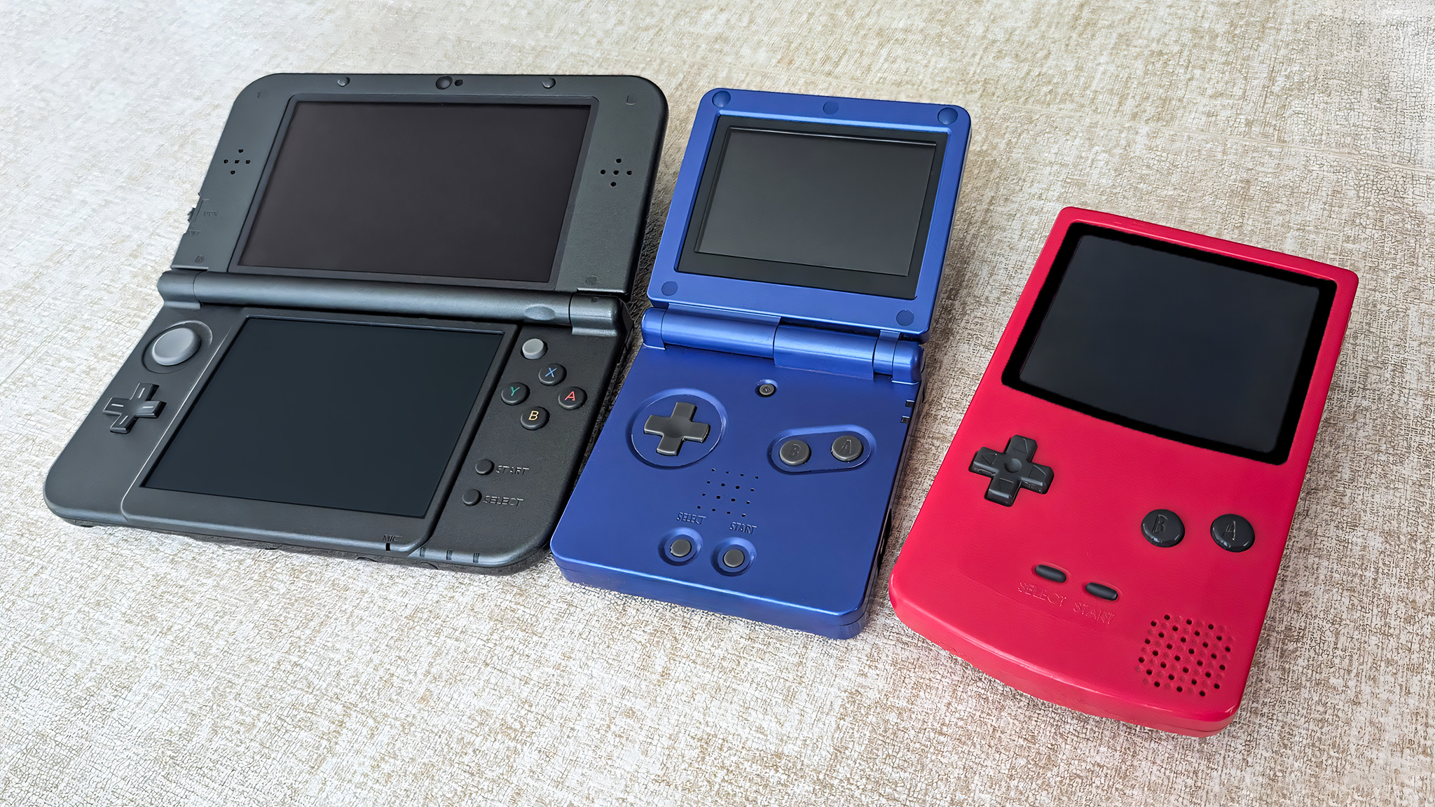 Three retro handhelds on a tan placemat.