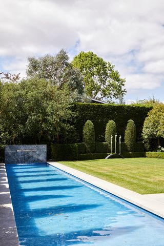 An example of pool patio ideas showing a rectangular swimming pool with a water feature and lawn