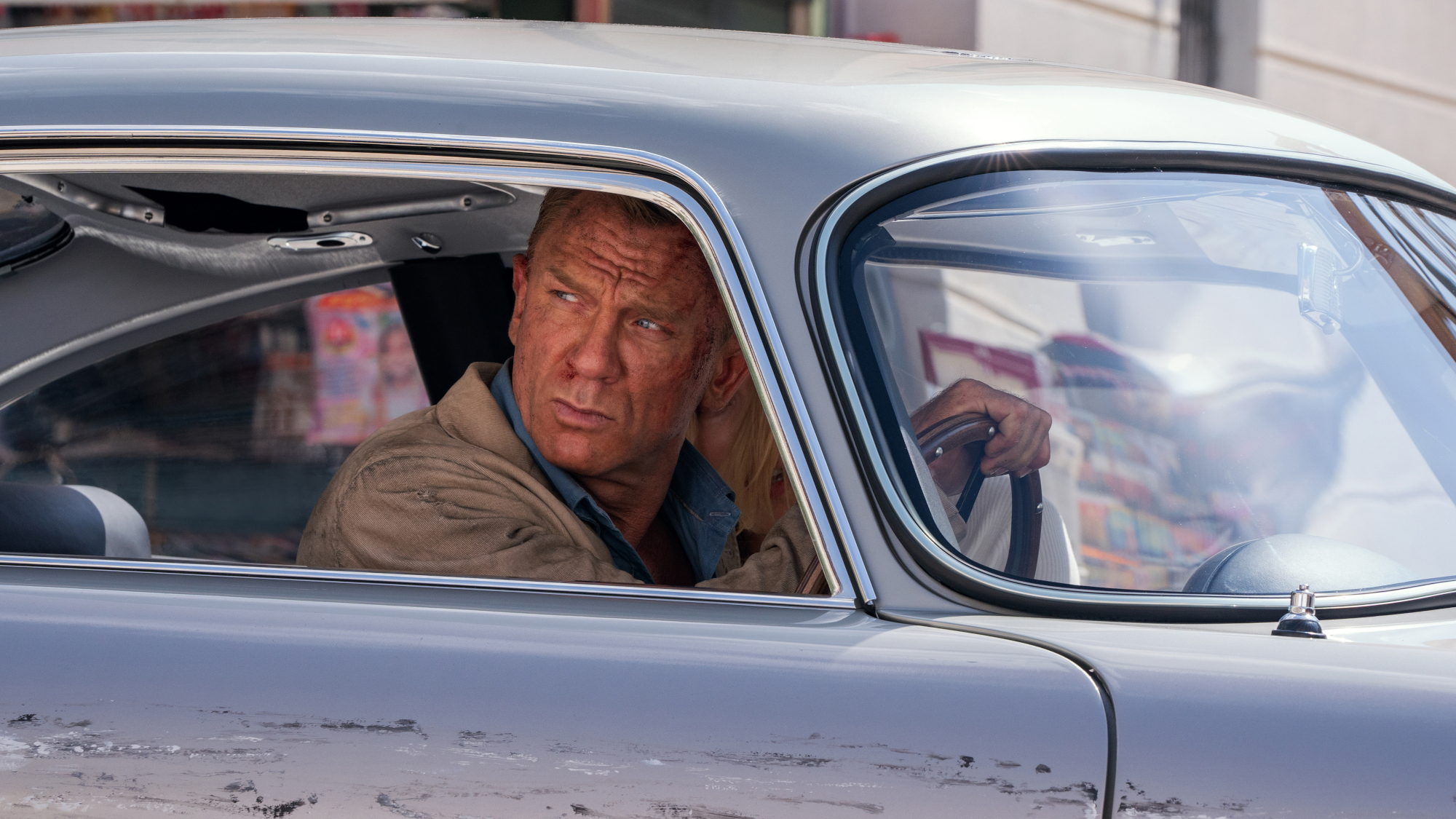 James Bond (Daniel Craig) drives in a damaged car in No Time to Die.